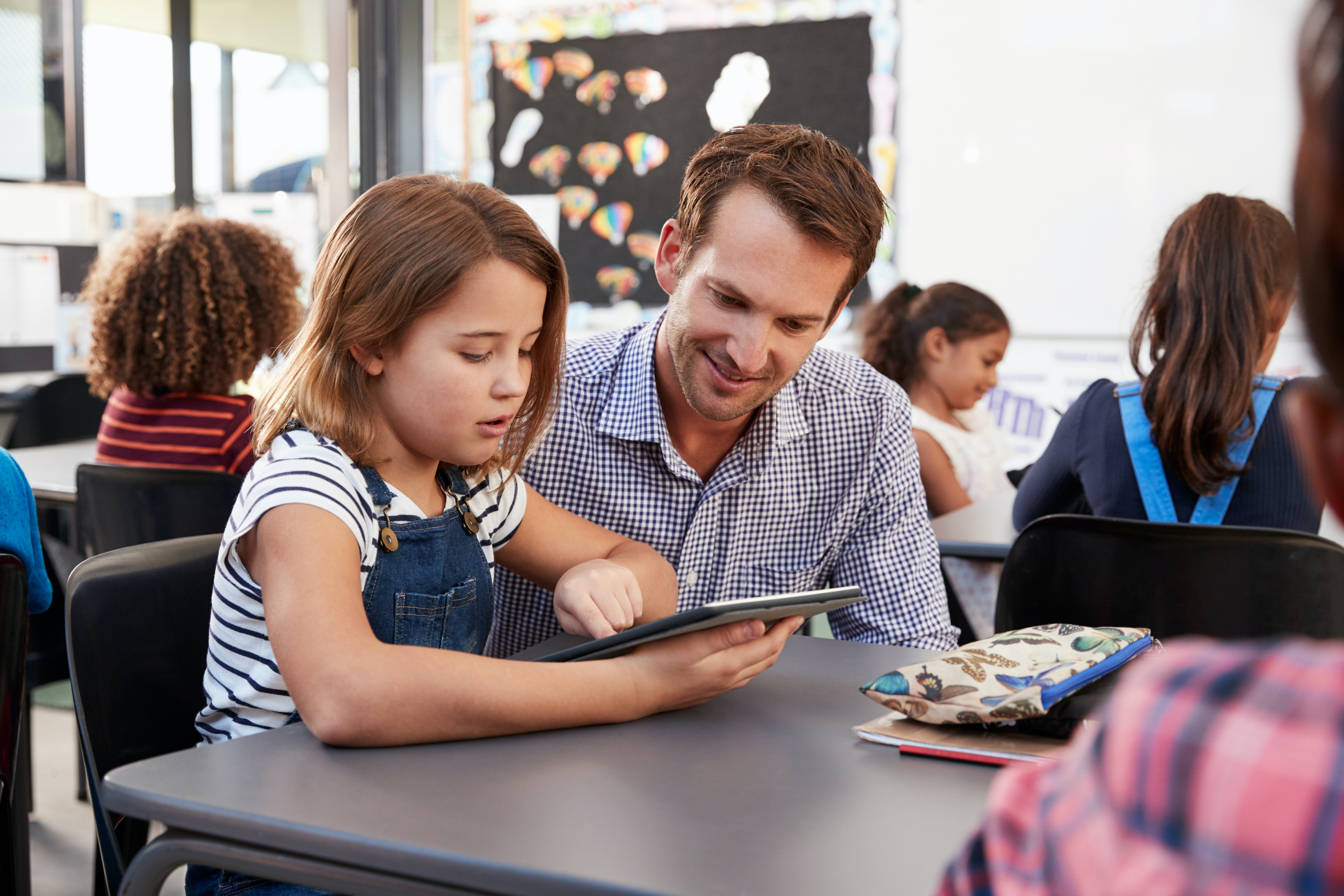 Here’s how weak policies on remote education have let our teachers down 2 Teacher and girl looking at computer tablet.